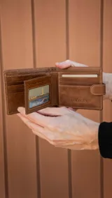Billetera de cuero marrón con presilla y broche a presión. El interior cuenta con un volante central con visor, múltiples tarjeteros y bolsillos, doble compartimento para billetes y un bolsillo interno con cierre en la parte posterior.