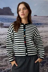 Cardigan de punto a rayas horizontales blancas y negras, con cuello redondo y cierre frontal de botones multicolor. Presenta mangas largas y diseño de corte recto.