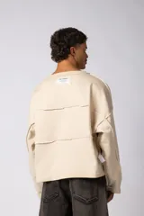 Buzo oversize de corte boxy, confeccionado en algodón rústico de alto gramaje en color beige. Presenta cuello redondo con borde crudo, mangas largas y una estampa frontal con el texto VCP delimitado por líneas horizontales blancas.