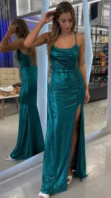 Vestido largo de fiesta color verde metalizado, con escote drapeado, tirantes finos cruzados en la espalda y diseño fruncido en el cuerpo. Posee una falda larga con abertura lateral pronunciada.