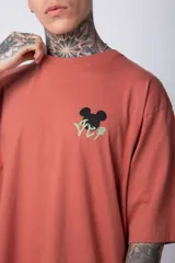 Remera negra de algodón de corte oversize, con mangas cortas y cuello redondo. Estampado pequeño en el frente y diseño grande en la espalda con Mickey Mouse y caracteres orientales en tonos rojizos.