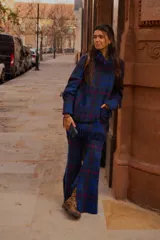 Sweater oversize de lana natural con estampado cuadrillé en tonos azul, verde y rojo. Presenta cuello alto, mangas largas y detalles de flecos torneados en el cuello, puños y dobladillo.