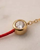Pulsera de hilo rojo de seda combinada con cadena de acero con baño de oro, con un dije redondo central tipo punto de luz engastado con circorias.