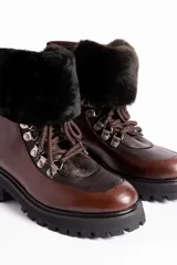 Borcegos de cuero vacuno en tonos marrón, con diseño de caña media y cuello con forro de piel sintética negra. Presentan cordones marrones, ganchos metálicos para ajuste y suela de goma tipo track con plataforma.