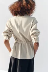 Chaqueta estilo safari color beige, con cuello de solapa tejido en crochet, manga larga, bolsillos delanteros con solapa y cintura ajustable con cordones. Cierre frontal con botones metálicos a presión.