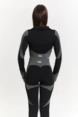 Conjunto deportivo de tres piezas compuesto por campera crop con cierre frontal, top y calza chupín. Presenta un diseño técnico con texturas combinadas en negro y gris, con detalles de paneles laterales rayados y tejido texturizado.