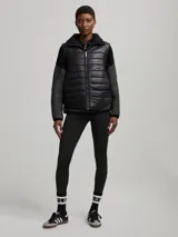 Chaleco negro capitoneado con cuello de piel sintética y cierre frontal con cremallera. Diseño sin mangas y corte recto.