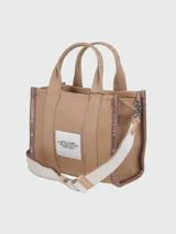 Bolso tipo tote de Marc Jacobs, confeccionado en tejido jacquard negro con detalles en color crema. Presenta el nombre del modelo estampado en el frente, doble asa superior y correa ajustable extraíble.