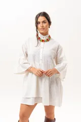 Vestido corto de broderie color crudo, con cuello camisero, cierre frontal parcial con botones, mangas tres cuartos acampanadas y corte evasé con volados.