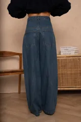 Pantalón jean gris de corte holgado, con cintura media, costuras redondeadas delanteras y traseras, y pliegues en la pierna.