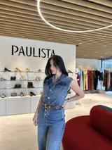 Enterito de jean azul con corte amplio, cuello camisero, sin mangas, con bolsillos delanteros y cierre frontal con botones.