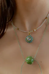 Gargantilla tipo bolo tie de tiento trenzado verde con dije esférico celeste con brillos incrustados.
