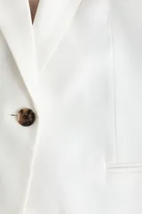 Blazer de botonadura sencilla con solapas de muesca, color blanco, de manga corta, con cierre de un botón y bolsillos delanteros ribeteados, con forro interno en tono tostado.