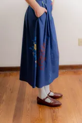 Falda midi de corte recto confeccionada en popelina de algodón, con diseño estampado floral en tonos azules y rojizos sobre fondo azul oscuro. Presenta un diseño con pinzas en la cintura y cierre frontal.