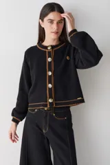 Cardigan de punto color marrón con detalles de ribete en color verde oliva en cuello, puños, ruedo y tapeta de botones. Presenta cierre frontal con botones grandes y un pequeño bordado en el pecho.