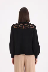 Sweater negro de punto con diseño de crochet en la parte superior del pecho y hombros, cuello redondo y mangas largas con puños ajustados.
