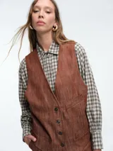 Chaleco estructurado de denim color terracota, con escote en V, cierre frontal con botones y bolsillos laterales tipo ojal.
