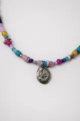 Collar corto con cuentas de piedra irregulares en tonos verde, marrón y blanco. Dije ovalado plateado con diseño en relieve.