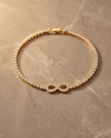 Pulsera de acero con baño de oro, diseño de infinito adornado con circonias y cadena tipo tenis.