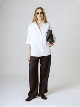 Camisa blanca de corte clásico, con cuello camisero y mangas largas con puños abotonados.