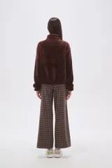 Buzo de polar tipo peluche color chocolate, con cuello alto y cierre frontal parcial. Presenta un bolsillo frontal con cierre y detalle de tela técnica en contraste.