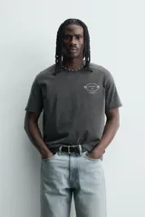 Camiseta de corte relajado con cuello redondo y mangas cortas. Presenta un efecto lavado que le otorga una apariencia única y estampados a contraste en el frente.