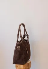 Cartera tipo tote de gamuza negra, con doble asa de mano y correa larga ajustable y desmontable. Cuenta con un diseño estructurado y base plana.