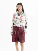 Camisa de seda color blanco con estampado floral y de dragones en tonos rojos, azules y verdes. Tiene cuello clásico, mangas largas con puños ajustables y botones forrados.