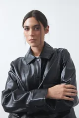 Chaqueta de cuero sintético negro con acabado brillante, cuello camisero, cierre frontal con botones a presión y bolsillos frontales con solapa.