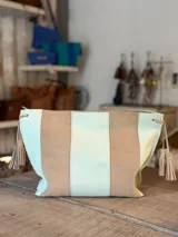 Cartera tipo sobre de cuero con diseño de rayas verticales en tonos verde menta y marrón tostado. Cuenta con detalles de borlas colgantes en los laterales.