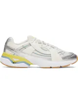 Championes deportivos UA Sola con diseño retro-futurista. Presentan una combinación de malla técnica y superposiciones sintéticas en tonos crema, con detalles en plateado metalizado, amarillo vibrante y azul claro. Incluyen entresuela de EVA acolchada y suela de goma color caramelo.