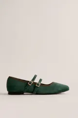 Zapato plano tipo Mary Jane de color verde oscuro, confeccionado en tela con textura estilo gamuza, punta fina y doble tira con hebillas metálicas doradas en el empeine.
