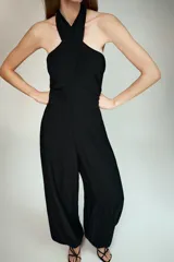 Mono largo de color negro con cuello halter cruzado y hombros descubiertos. Presenta un diseño de piernas tipo bombacho con bajos ajustables mediante lazadas y cierre lateral oculto.