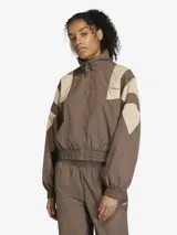 Campera deportiva Adidas de corte oversize, con cierre frontal completo y cuello alto. Presenta un diseño de bloques de color en tonos marrón y beige, inspirado en el estilo Equipment de los años 90, con puños y cintura elásticos.
