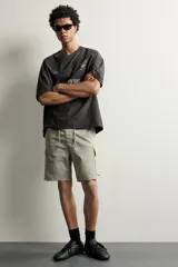 Bermuda cargo color negro de corte relaxed fit, confeccionada en tejido de algodón con elasticidad y efecto lavado. Cuenta con cintura elástica ajustable con cordón, bolsillos frontales y bolsillos laterales tipo cargo con solapa en las perneras.