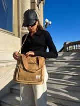 Cartera tipo tote bag color beige, confeccionada en lona resistente. Cuenta con doble asa de mano, correa larga ajustable y extraíble, cierre principal y bolsillo frontal con cierre.