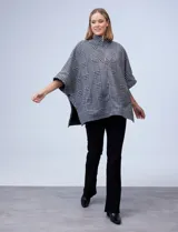 Poncho de tejido soft con estampado de cuadros, cuello alto y cierre frontal parcial. Presenta diseño holgado con mangas amplias y bolsillos laterales.