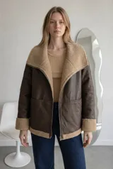 Campera tipo gamulán de cuero sintético marrón con interior y detalles de corderito beige. Presenta cuello solapa amplio, cierre frontal con cremallera metálica, mangas largas con puños de corderito y bolsillos frontales.