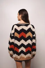 Buzo tejido a mano en lana merino, con diseño de patrón en zigzag multicolor en tonos crema, negro, azul y tostado. Presenta un corte holgado, cuello redondo y mangas largas con puños acanalados.