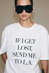 Camiseta blanca de manga corta y cuello redondo, de corte regular fit, con detalle de texto estampado en negro en el frente.