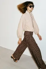 Pantalón de tiro alto con pernera ancha y diseño fluido. Presenta un estampado de lunares blancos sobre fondo marrón y detalle de frunces en la cintura.