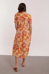 Vestido midi con estampado de círculos concéntricos en tonos naranja, amarillo y blanco. Tiene cuello camisero, mangas cortas y cinturón de la misma tela.
