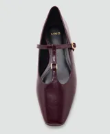 Zapato plano tipo Mary Jane, color bordó, de punta fina y tira en forma de T con hebilla metálica dorada ajustable.