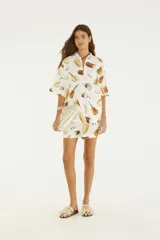 Camisa oversize blanca con estampado de instrumentos musicales, cuello camisero, botones frontales, hombros caídos y mangas cortas amplias.