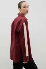 Camisa de corte holgado y largo medio, color negro con detalle de franja lateral en color crema a lo largo de las mangas. Presenta cuello clásico, cierre frontal con botones y tajos laterales en el ruedo.