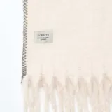 Bufanda de tejido suave color beige, con flecos en los extremos y detalle de costura decorativa en zigzag a lo largo de los bordes.