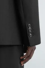 Blazer de corte regular confeccionada en tejido de lana italiana. Presenta cuello con solapas de pico, cierre frontal de botonadura cruzada, manga larga con puños abotonados, bolsillos de vivo en el pecho y bolsillos de solapa en la cadera.