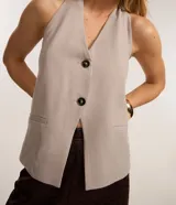 Chaleco color beige con escote halter, corte al cuerpo y cierre frontal con botones. Presenta un bolsillo de ojal en el frente.