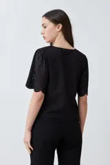 Blusa negra de broderie con escote en V y lazos para atar en el frente. Tiene mangas cortas con terminación de puntilla. 