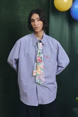 Camisa de corte oversize con estampado a rayas verticales en tonos azul y blanco, cuello clásico y cierre frontal con botones.